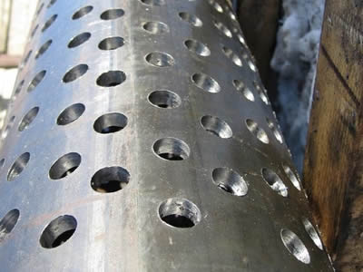 A perforated pipe with round holes in staggered rows is lying on the side of wall.